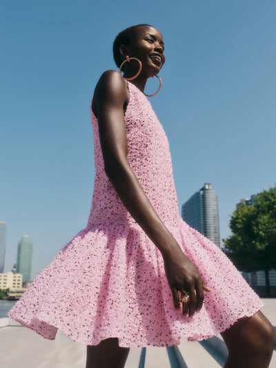 The model is wearing a pink speckled mini dress with a drop-waist silhouette and a voluminous flounce skirt. 
