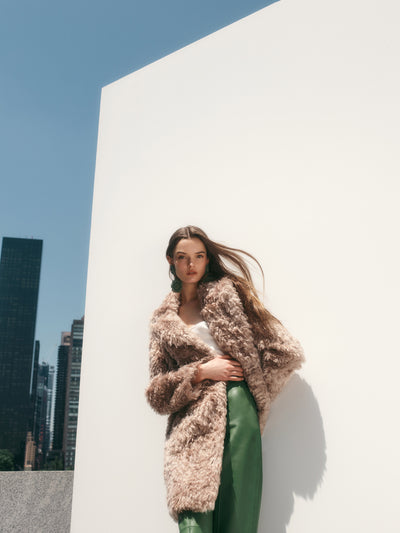 The model is wearing a wool-blend coat and green leather pants. 