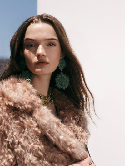 The model is wearing green floral earrings and a green pave crystal necklace. 