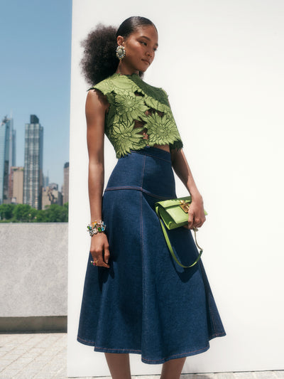 The model is wearing a green sleeveless top with floral cutouts and a denim midi skirt. 