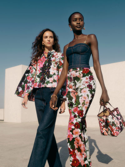 Two models are standing next to each other. The model on the left is wearing a Hollyhock jacket and denim pants. The model on the right is wearing a denim bustier, hollyhock pants, and is carrying a hollyhock bag. 