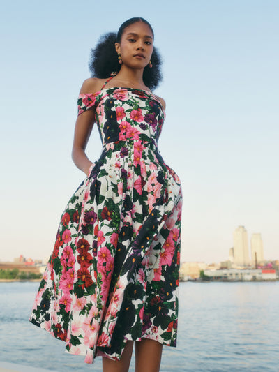 The model is wearing an off-the-shoulder midi dress with self-tie halter straps and asymmetrical neckline and showcases the hollyhocks motif.