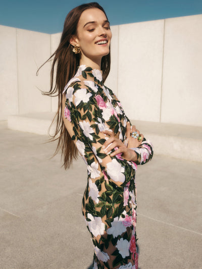 The model is wearing a long sleeve tulle gown with oversized applique white and pink flowers. 