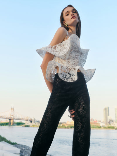 The model is wearing a white lace, ruffled halter-neck top and black lace pants. 