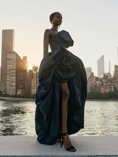 The model is wearing a strapless black gown against the New York City skyline. 