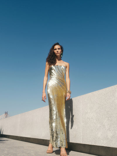 The model is wearing a gold, sequin embellished gown. 