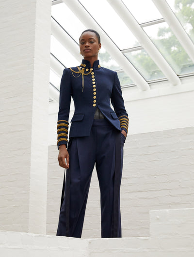 A model wears a military like jacket with gold details and matching navy pants
