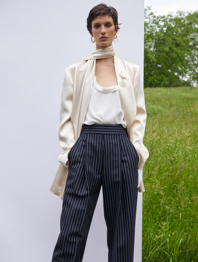 A model wears striped, black pants with a white top and cream blazer and scarf