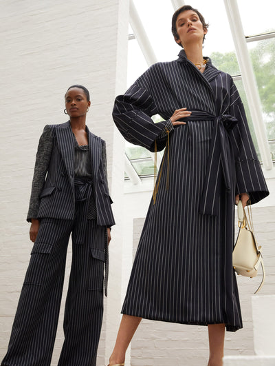 Two models; the model on the left wears a striped, black suit set and the model on the right wears a black striped coat