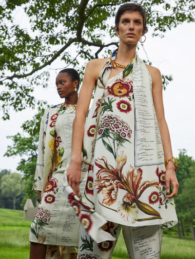 Two models both wearing the same print with flowers and script; the model on the left wears it in dress form and the model on the right wears it in a top and pant form
