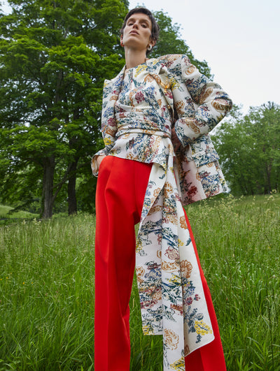 A model wears red pants with a red blue, yellow embroidered red top and matching jacket