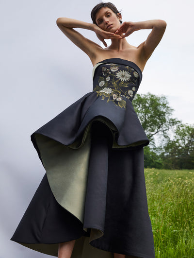 A model wears a black and green ruffle gown with embroidered flowers