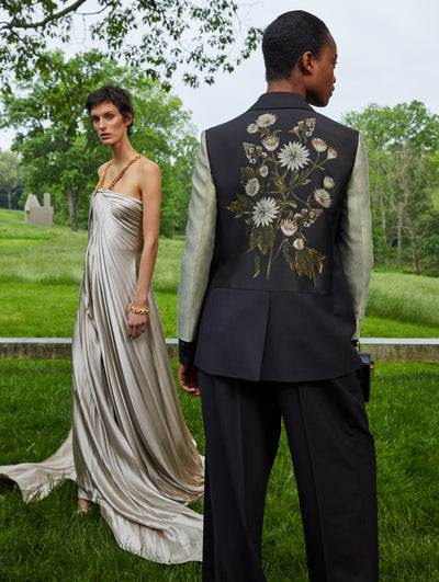 Two models; the model on the left wears a silk grey gown and the model on the left wears a suit set with flowers embroidered on the back