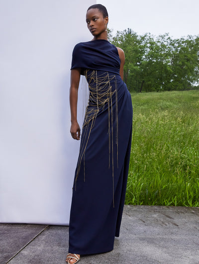 A model wears a one shoulder black gown with gold details