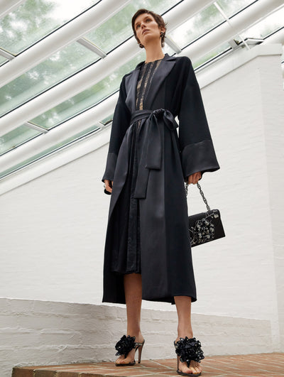 A model wears a black silk coat and lace dress