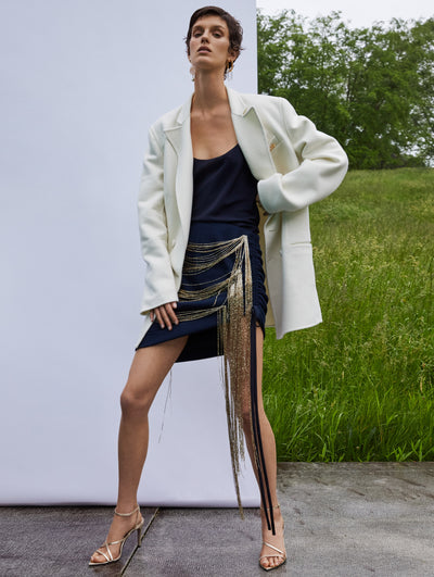 A model wears a black dress with gold details and white blazer