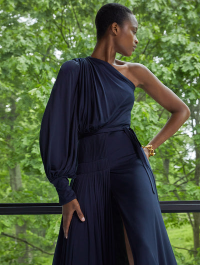 A model wears a one shoulder black blouse with ruched details and black pants