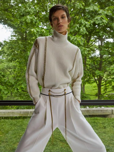 A model wears white pants and cardigan with gold details