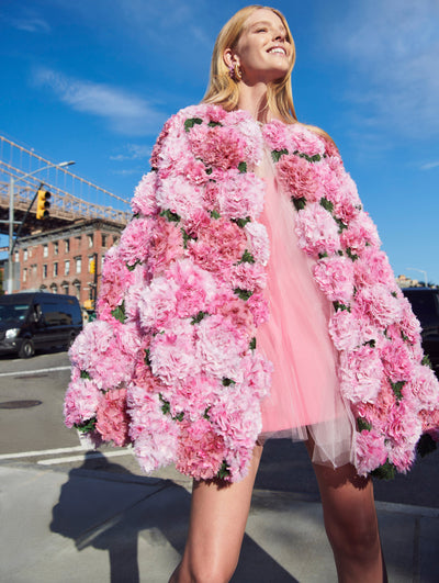 A model poses outside in an Oscar de la Renta pink hydrangea embroidered cape coat. 