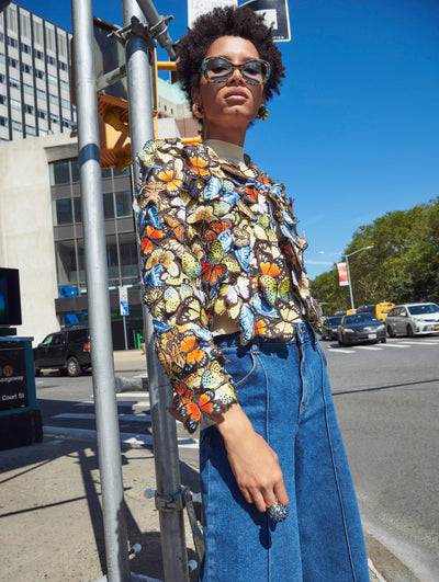 A model poses outside in an Oscar de la Renta butterfly embroidered jacket styled with denim jeans. 