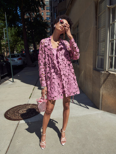 A model poses outside in an Oscar de la Renta pink leather laser-cut floral jacket paired with a crystal pave pink bucket bag. 