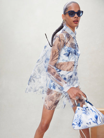 A model poses inside in an Oscar de la Renta see-through floral blouse with a matching handbag. 