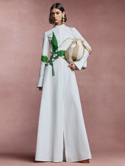 The model is wearing a long sleeved, white caftan with the Lily of the Valley flower across the front. 