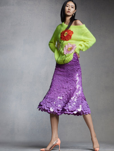 The model is wearing a purple paillette embroidered skirt with a knit sweater adorned with painted poppies. 