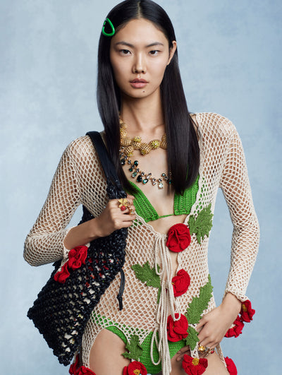 The model is wearing a white, long-sleeved crochet coverup adorned with red crochet flowers. 