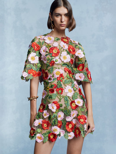 The model is wearing a mini dress adorned with multicolor poppy flowers. 