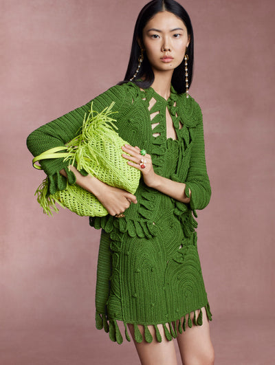The model is wearing a matching green crochet dress and jacket with a green raffia bag. 