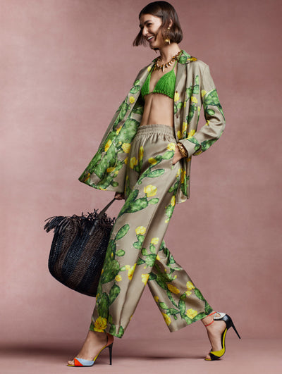 The model wears a matching silk set with a green and yellow cactus print against a pink background. 