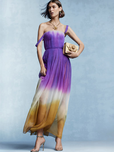 The model is wearing a purple ombre cocktail dress with a gold rose necklace. 