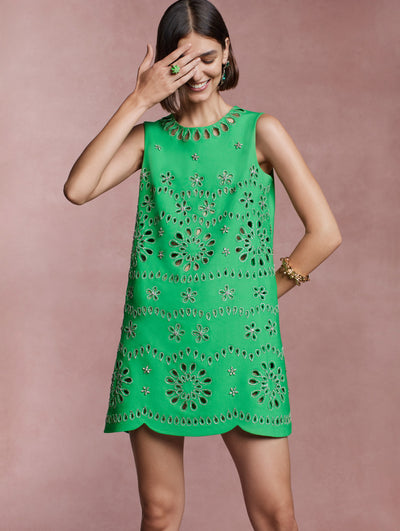 The model is wearing a green shift dress with crystal eyelet detailing. 