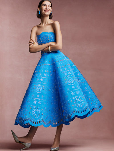 The model is wearing a blue strapless evening gown with crystal eyelet detailing. 
