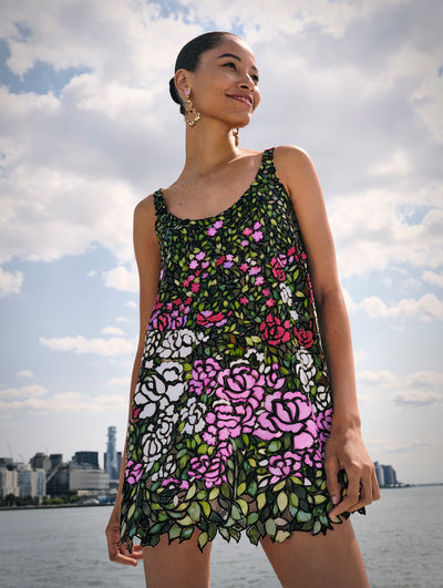 The model poses against the New York City skyline in the signature stained glass technique in an English rose mini dress from Oscar de la Renta's Spring 2025 collection. 