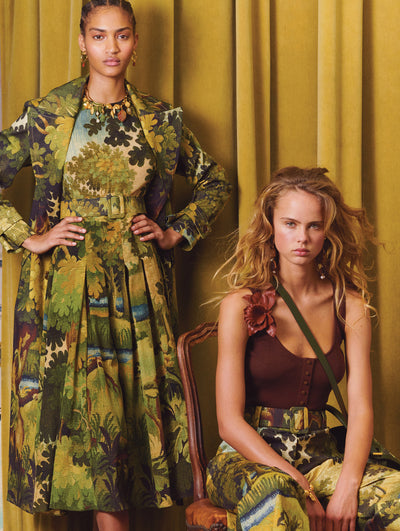 Two models; the model on the left wears a matching dress and jacket with an embroidered landscape motif and the model on the right wears a brown top with the same print in pants form