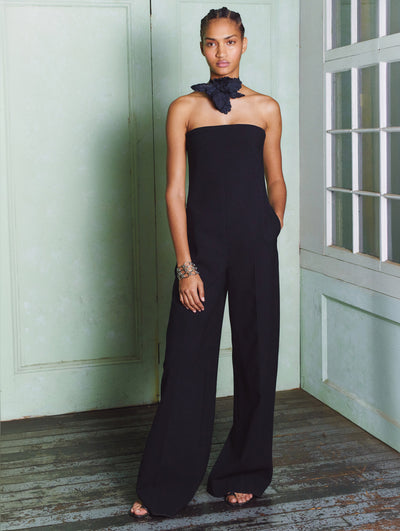 A model wears a black pantsuit with a flower necklace