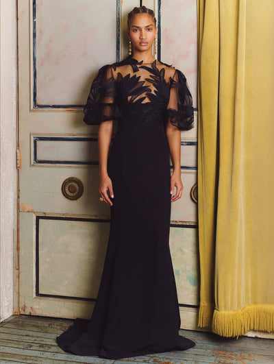A model wears a black gown with lace and flowers embroidered on the top