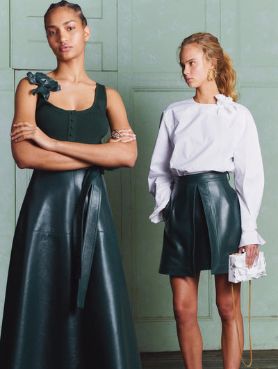 Two models, the model on the left wears a leather skirt and black top the model on the right wears a leather skirt and white blouse