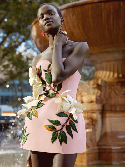 A model poses in front of a fountain wearing an Oscar de la Renta pink embroidered cocktail dress. 