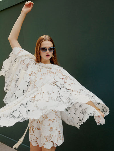 A model lifts here arms in an Oscar de la Renta white lace blouse and short set. 