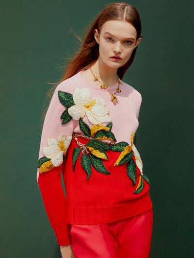 A model wears an Oscar de la Renta pink and red floral embroidered sweater with red trousers. 