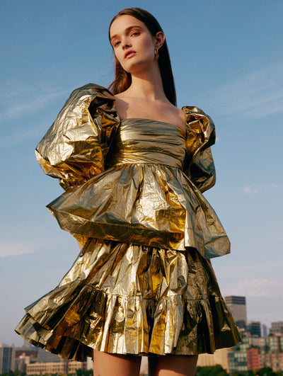 A model poses outside in an Oscar de la Renta gold metallic cocktail dress.