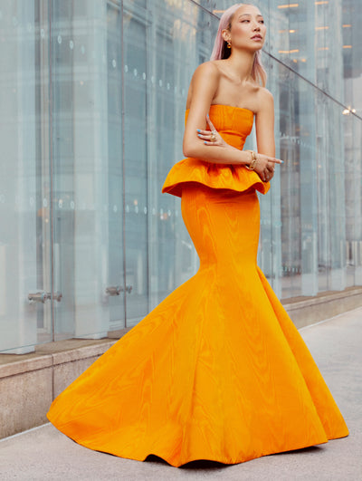 A model poses outside in an Oscar de la Renta orange peplum gown. 