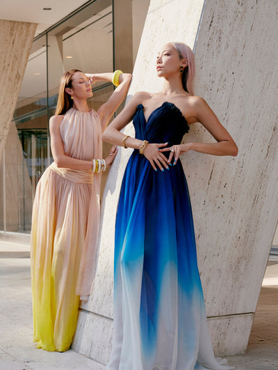 Two models wear Oscar de la Renta ombre gowns outside of a building. 