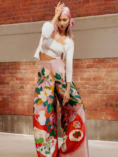 A model poses against a wall in an Oscar de la Renta white cardigan and printed floral trousers.
