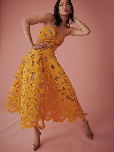 The model poses with a pink backdrop wearing a yellow strapless lace dress from Fall 2021 