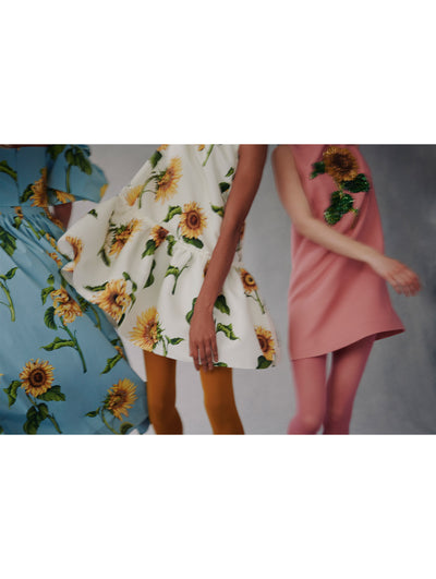 Three models twirl while wearing fall 2021 sunflower dresses in blue, white, and pink.