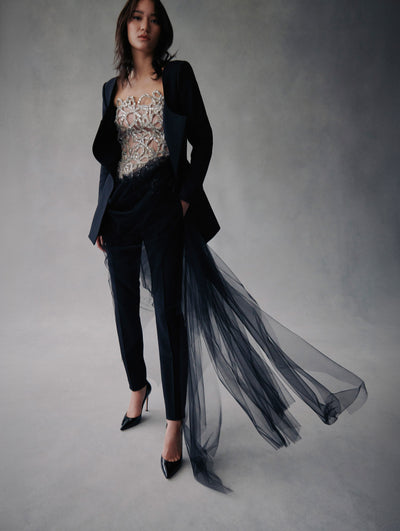 The model wears a crystal bow embellished corset with black pants and a black coat with tulle in the bottom from Fall 2021.